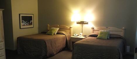 Een hotelkamer met twee eenpersoonsbedden, een nachtkastje met een lamp, een telefoon en een stoel.