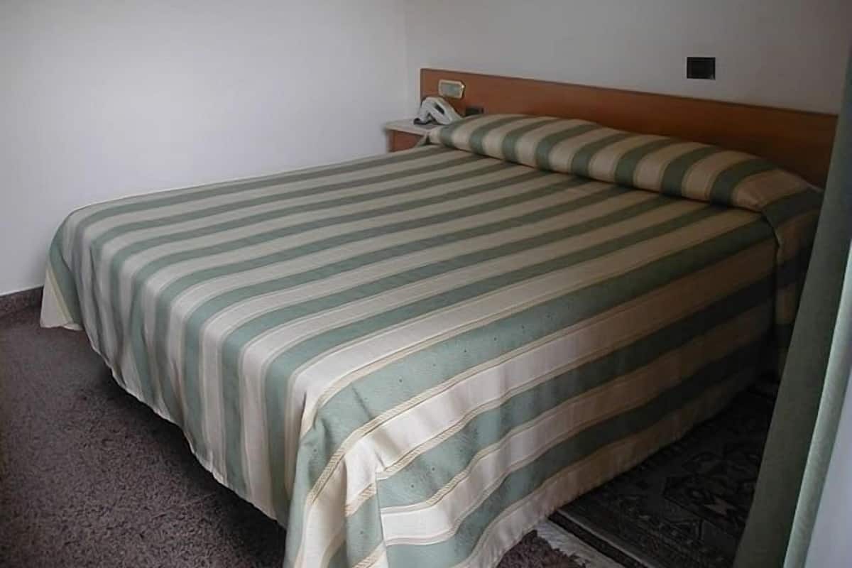 Een enkel bed met een gestreept dekbedovertrek in een kamer met een effen muur en een ingelijste foto boven het bed.