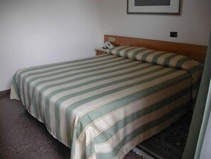 Ein Einzelbett mit einem gestreiften Bettüberwurf in einem Zimmer mit schlichter Wand und einem Bild, das über dem Bett hängt.