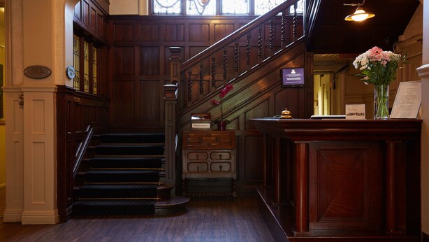 A grand staircase with wooden railings and a chandelier, leading to an office area with a reception desk and a vase of flowers. - The Lismoyne Hotel (Fleet)