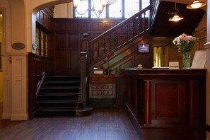 A grand staircase with wooden railings and a chandelier, leading to an office area with a reception desk and a vase of flowers. - The Lismoyne Hotel (Fleet)