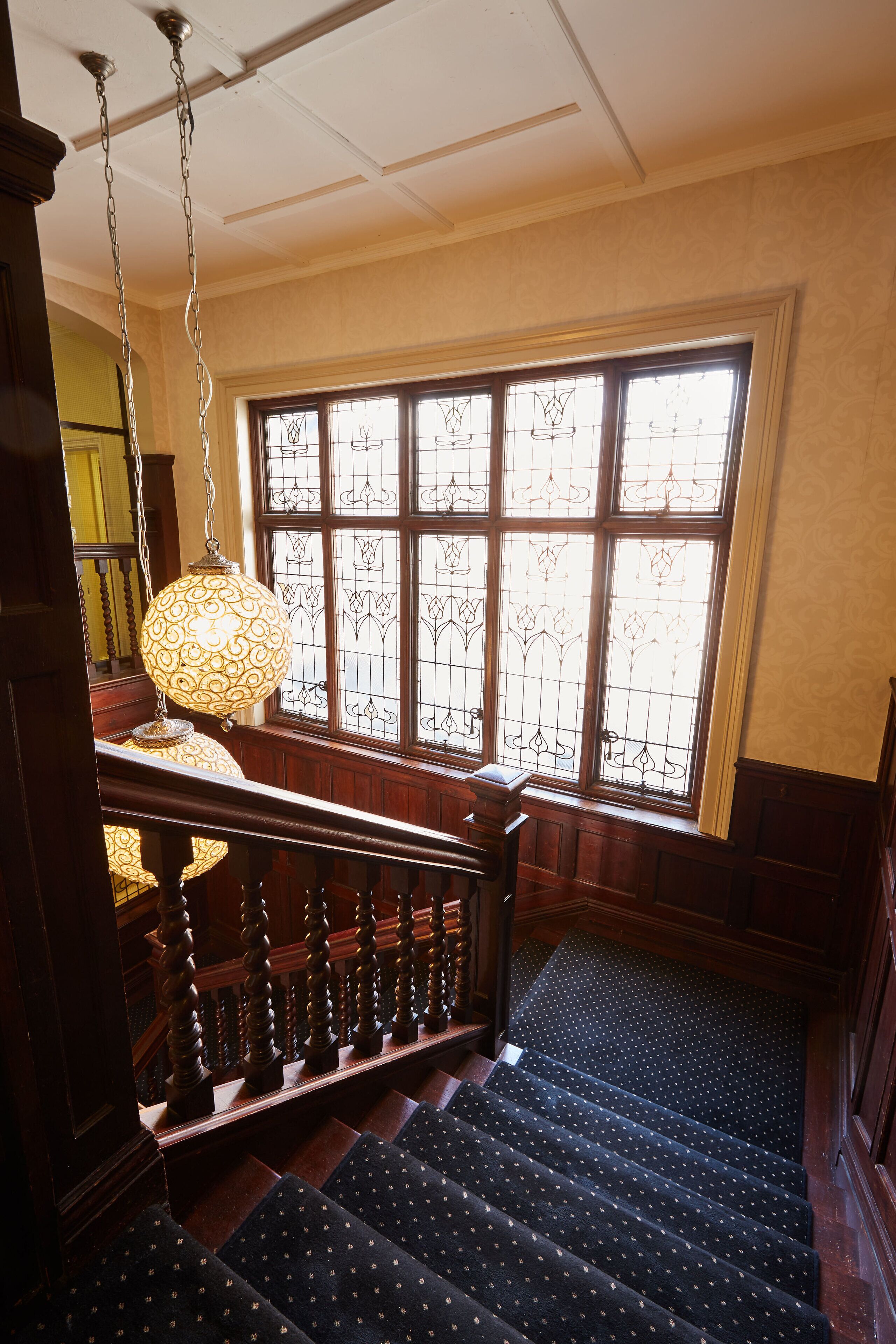 A staircase with a patterned carpet, a wooden railing, and a large window with decorative glass.
