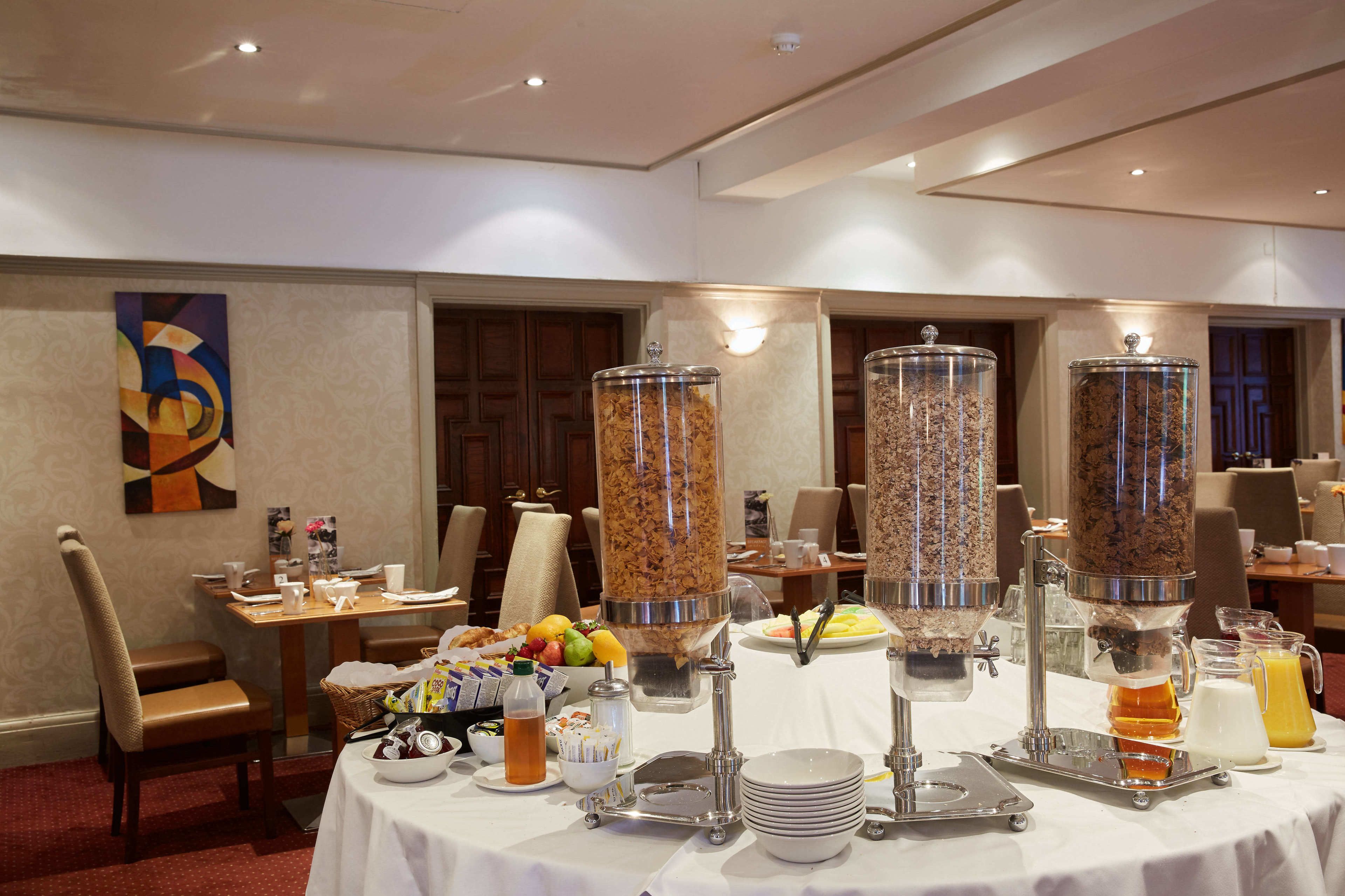 Buffet d'esmorzars amb diversos distribuïdors d'aliments, un bol de fruita i un dispensador de suc.