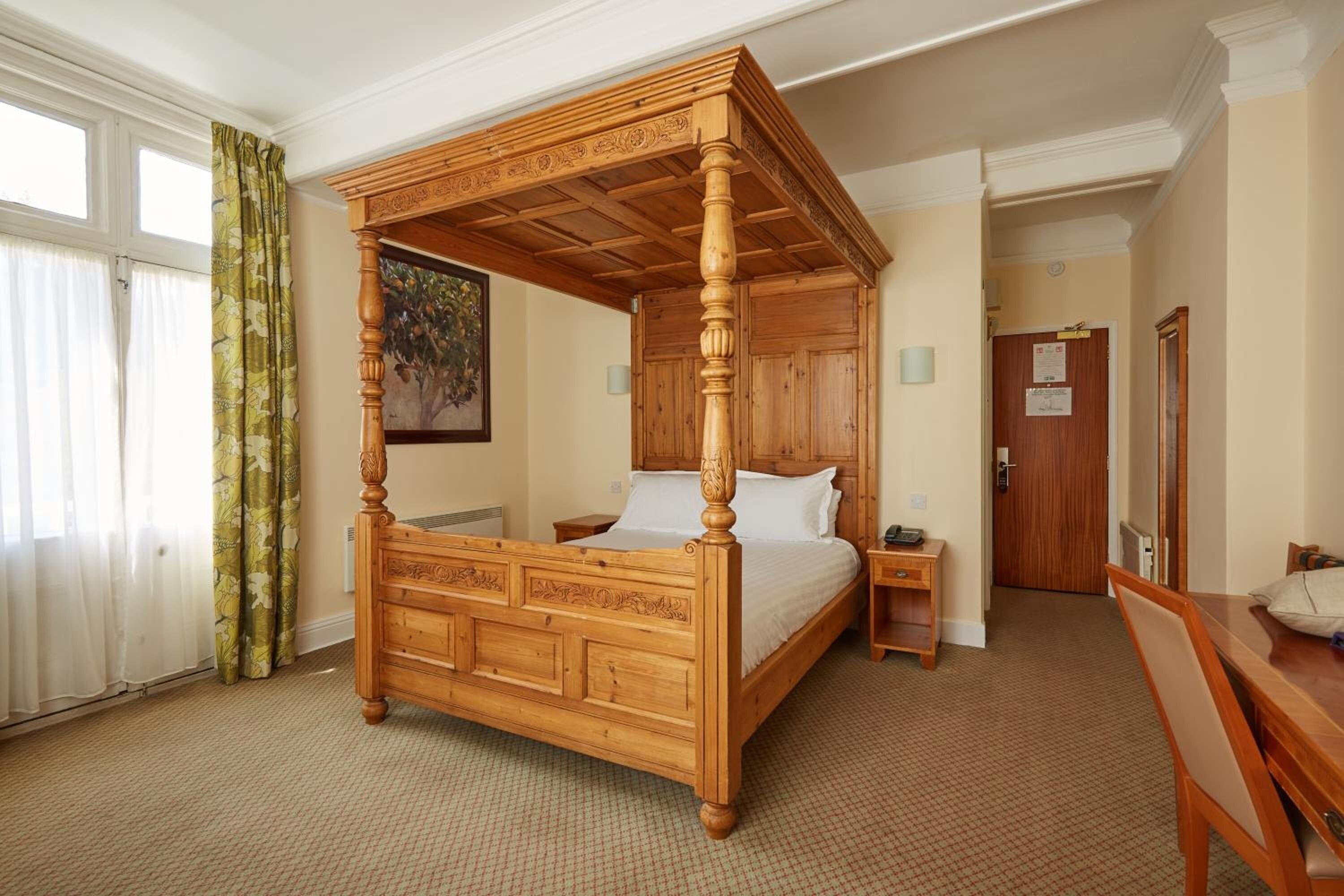 A four-poster bed with a wooden headboard, a bedside table, and a chair.