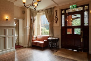 Quarto com sofá de couro, piso de madeira, um lustre e uma porta com sinalização de saída verde.