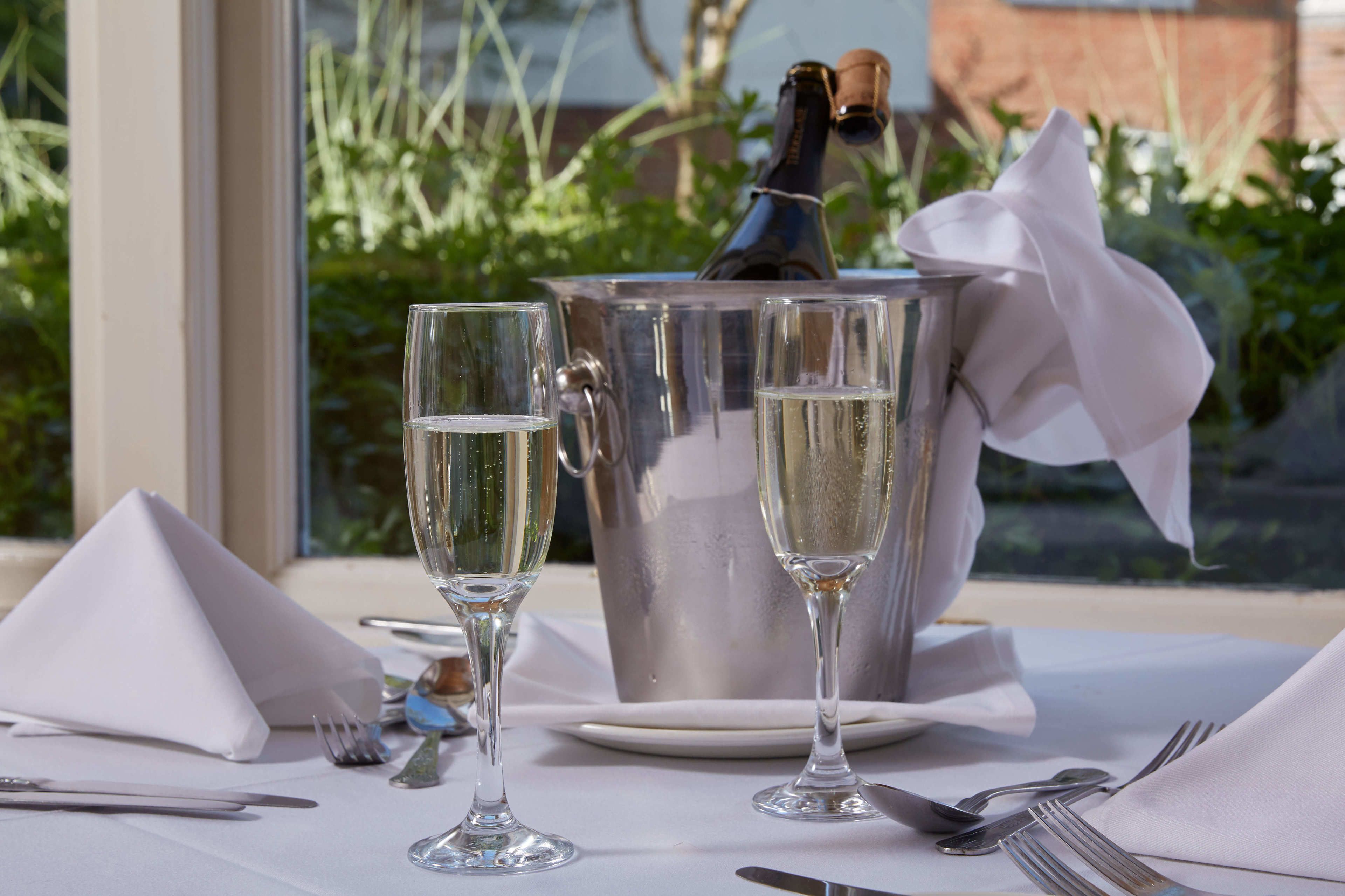 Ett bord dukat med två champagneglas, en silverfärgad isspån och en flaska champagne.