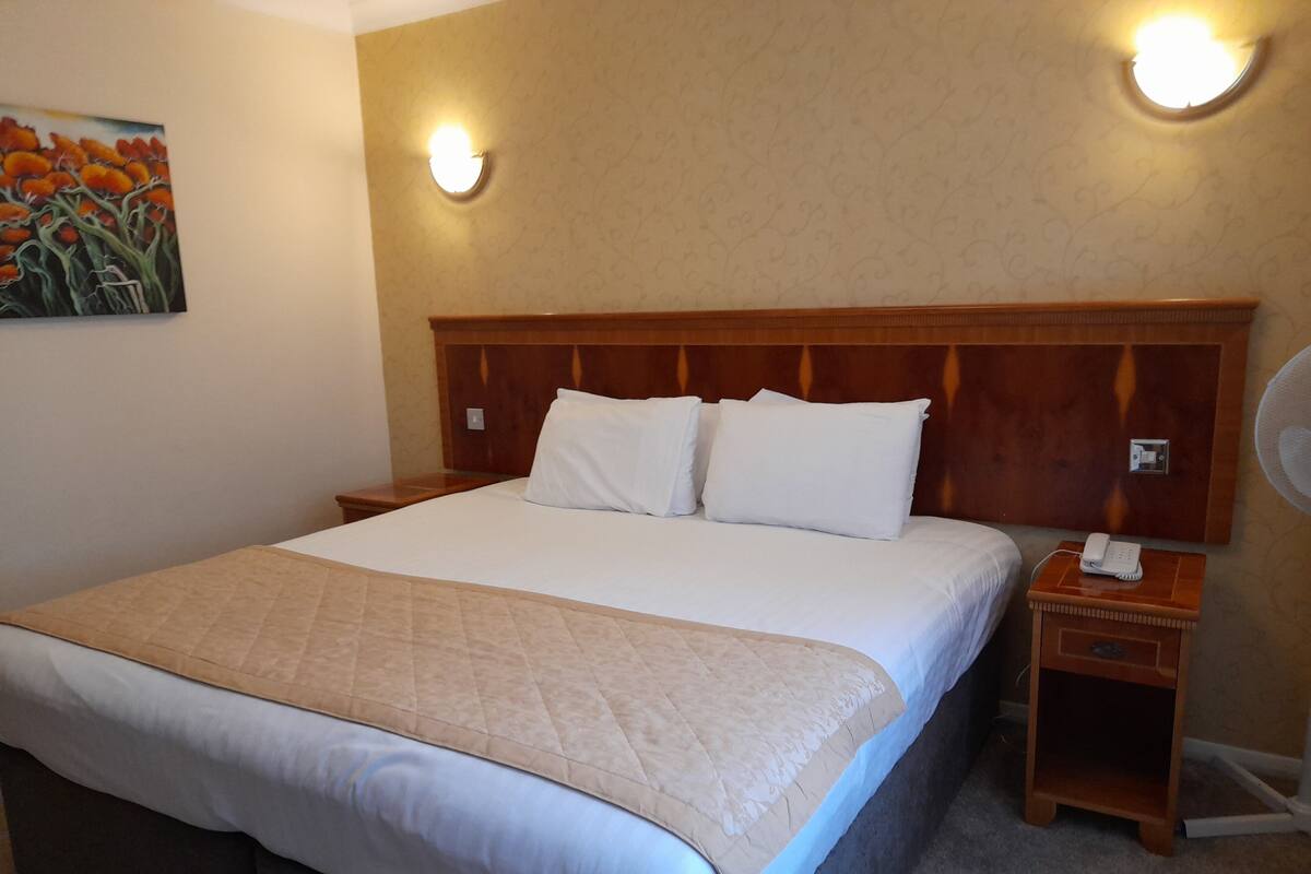 A hotel room with a large bed, two bedside tables, a nightstand with a phone, and a wall-mounted light fixture.