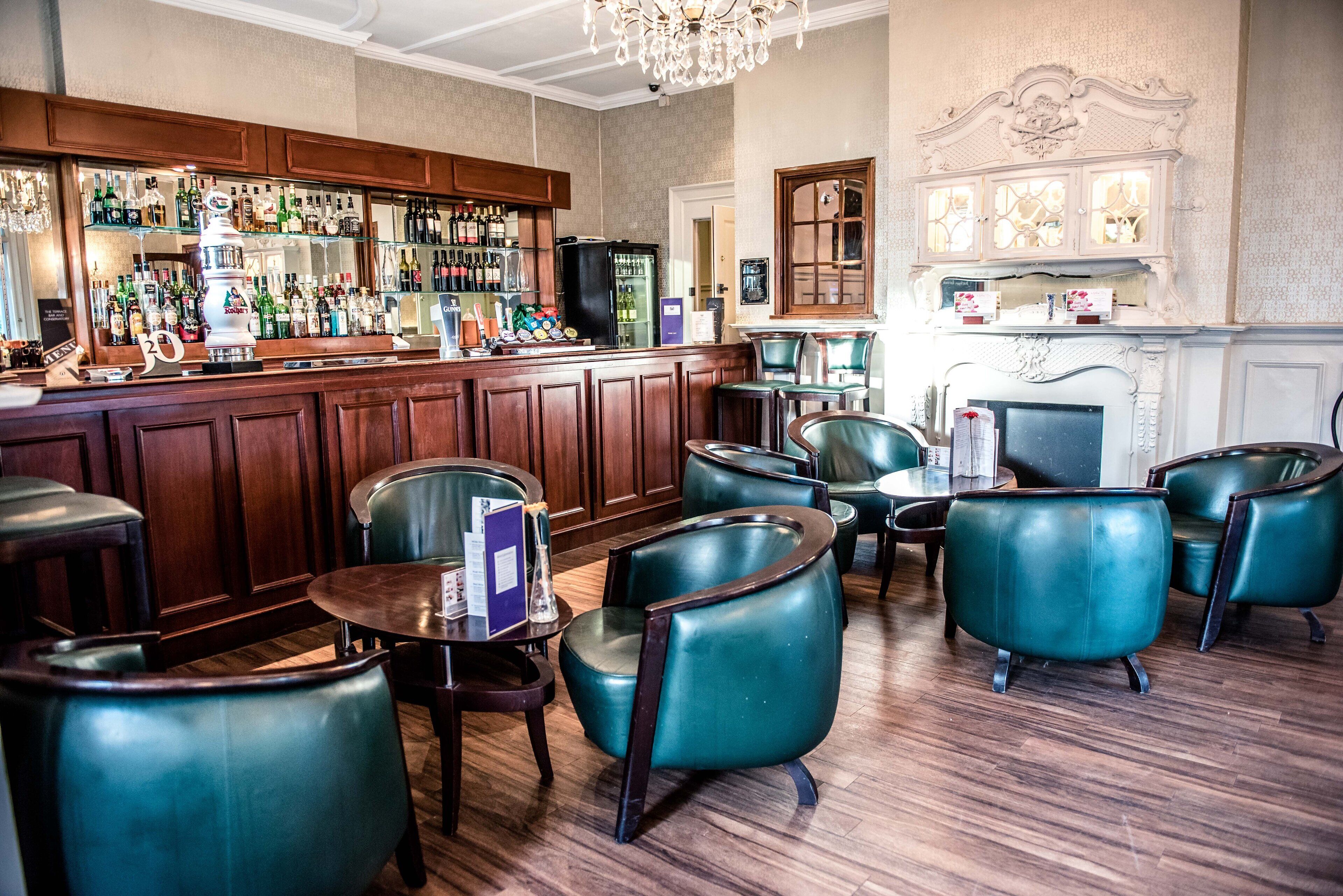 A bar area with wooden cabinets, a variety of bottles, and teal leather chairs.