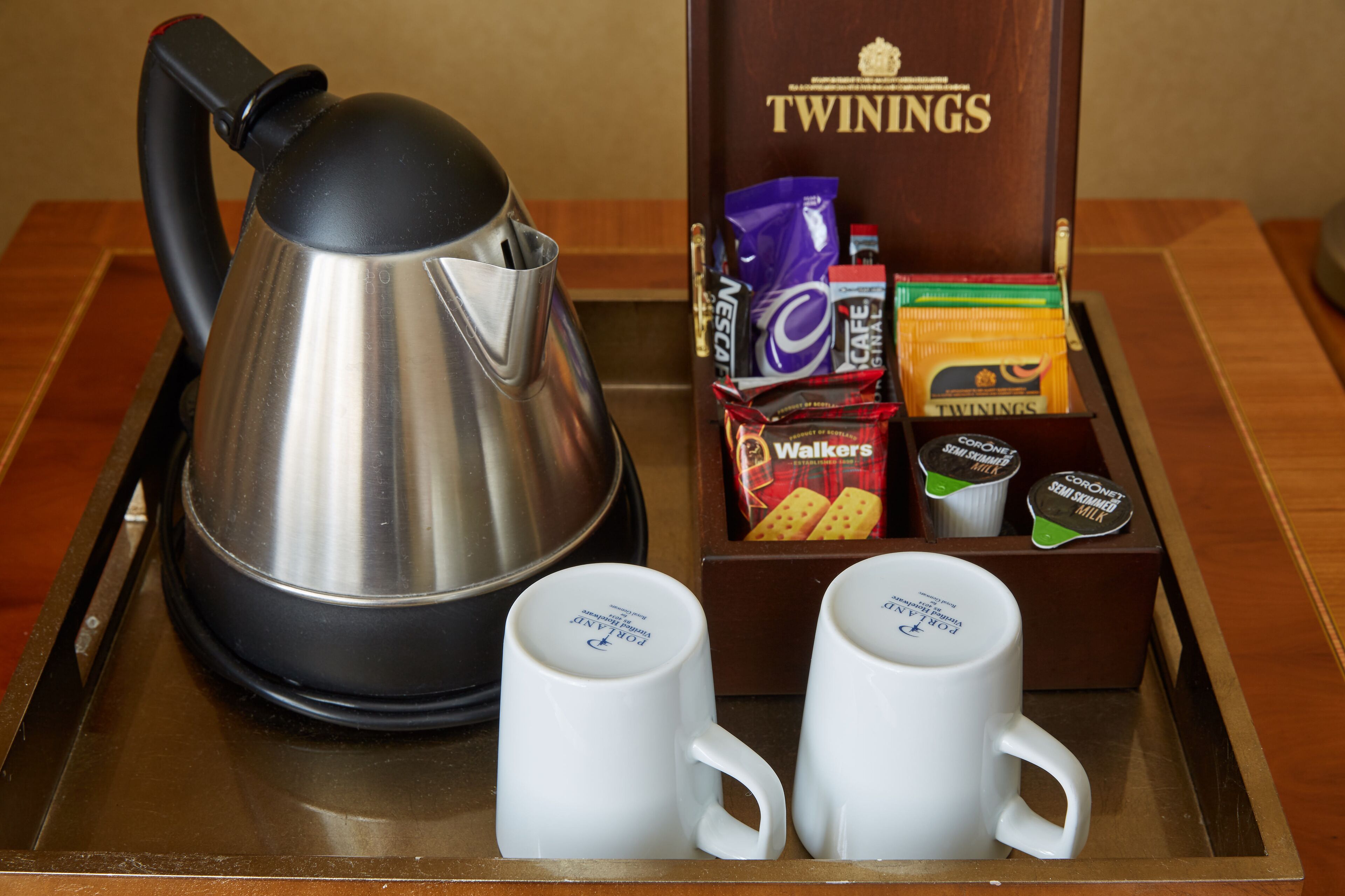 A tray with a kettle, two coffee mugs, and a box of Twinings tea.