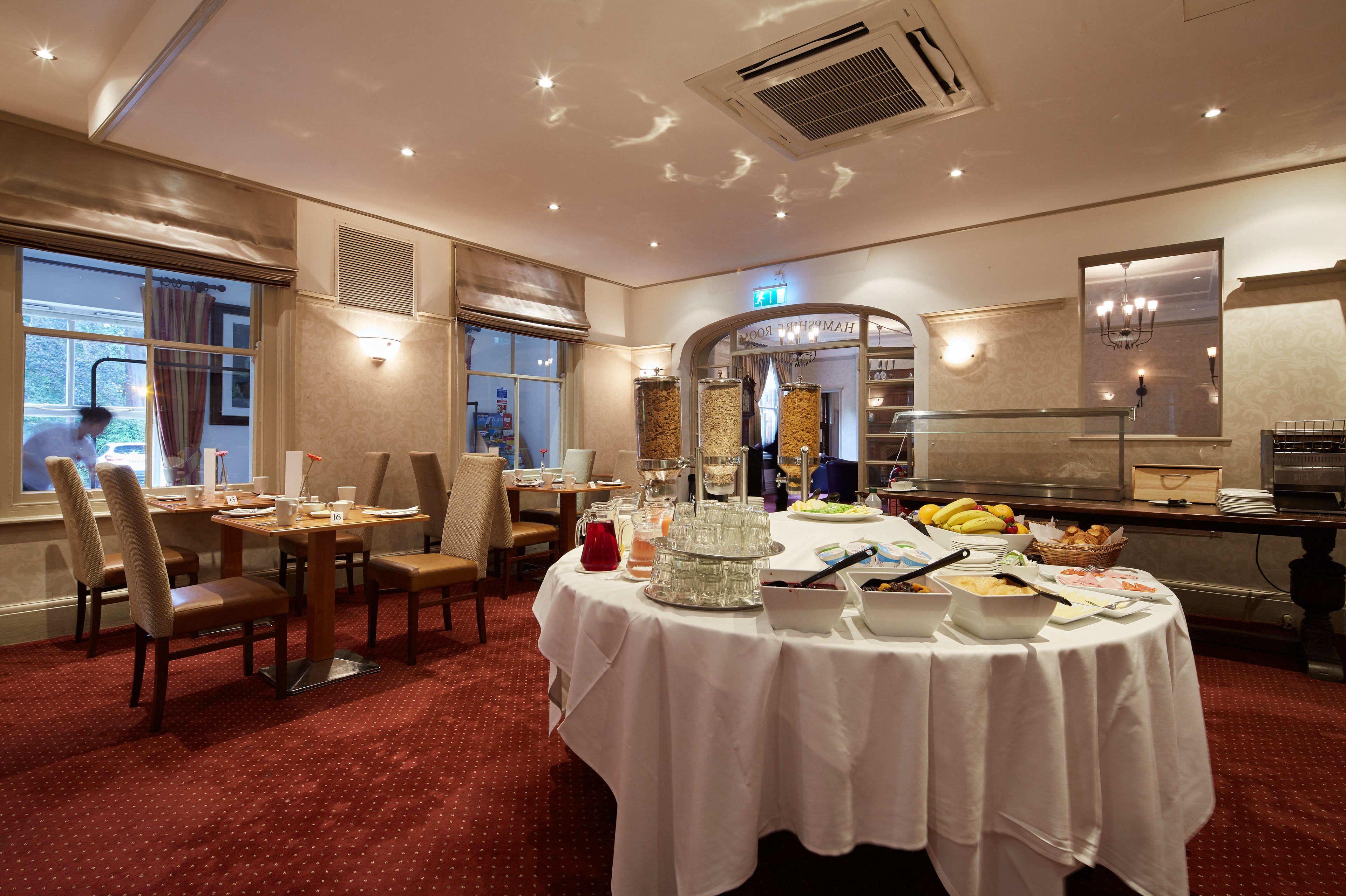 A hotel dining area with round tables, chairs, and a buffet setup.
