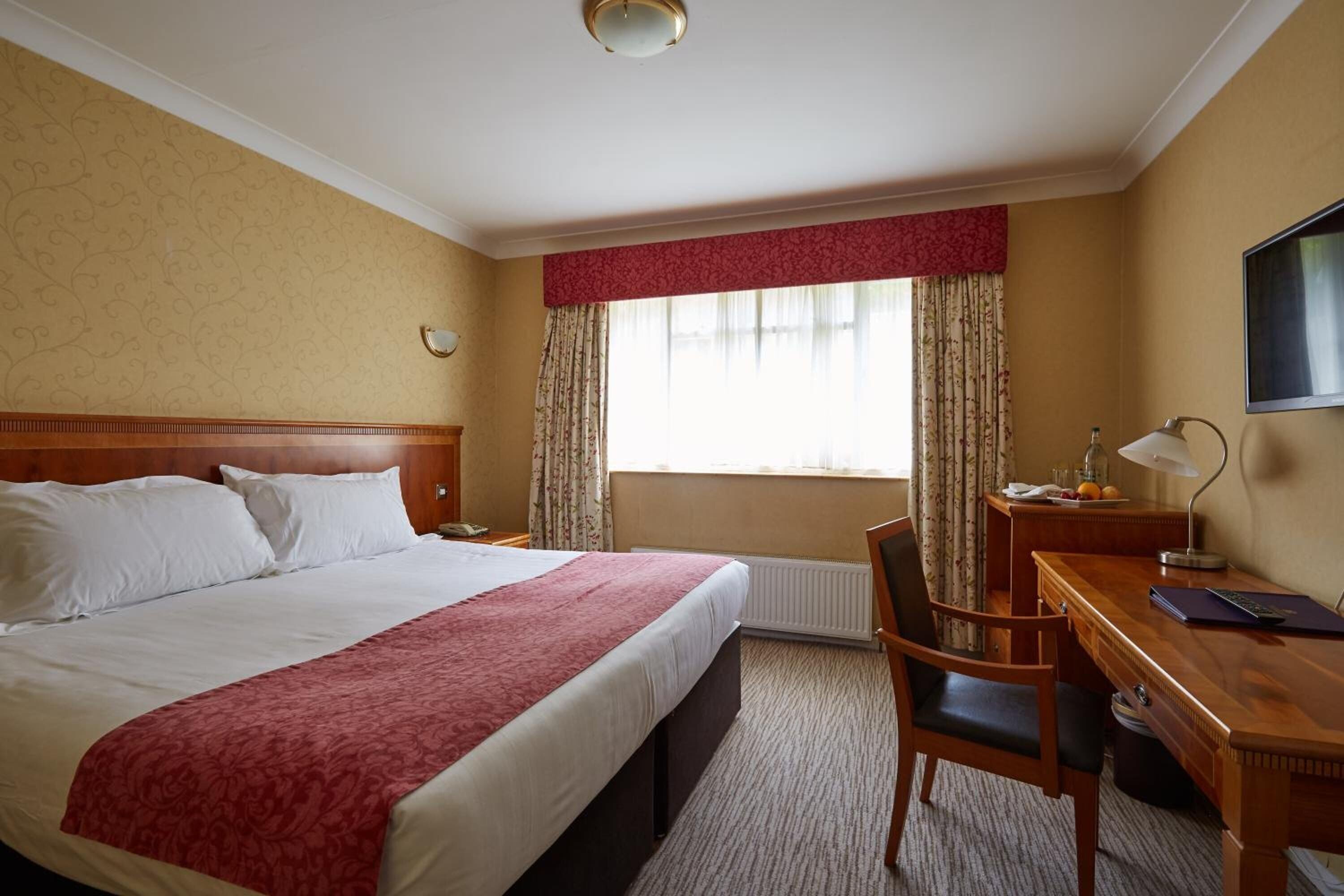 A hotel room with a large bed, a desk with a chair, a television, and a window with curtains.