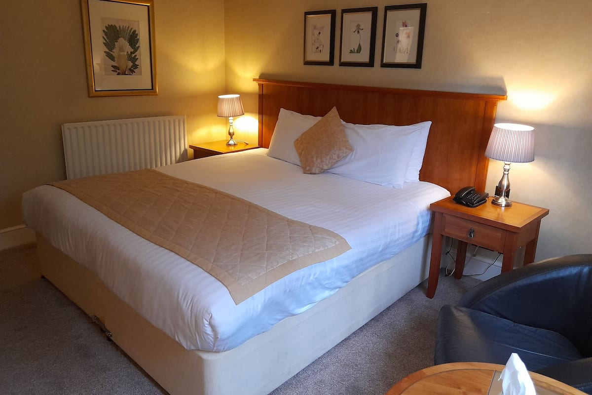 A hotel room with a large bed, two bedside tables, a chair, and three framed pictures on the wall.