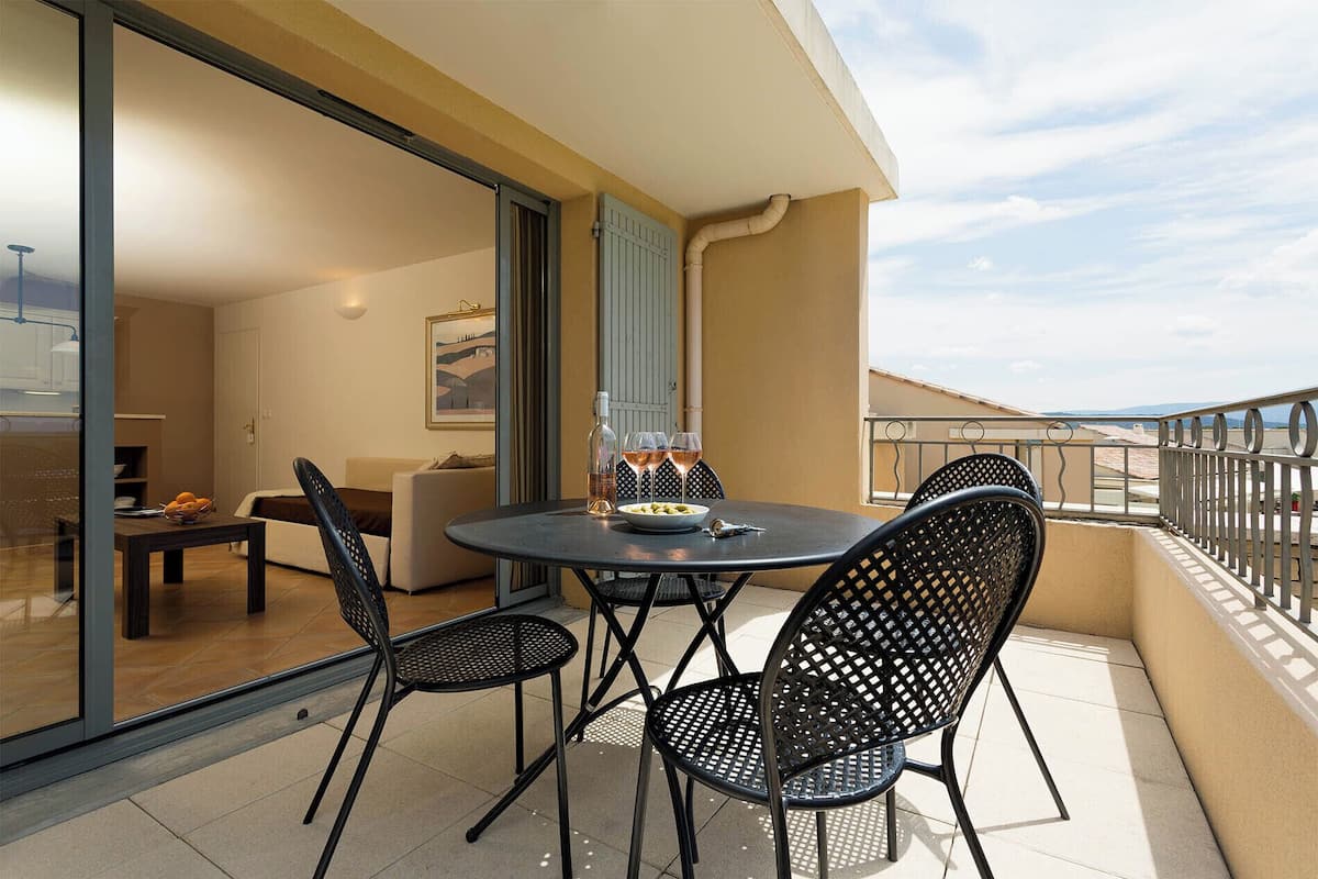 A balcony with a round table, four chairs, and a bottle of wine.
