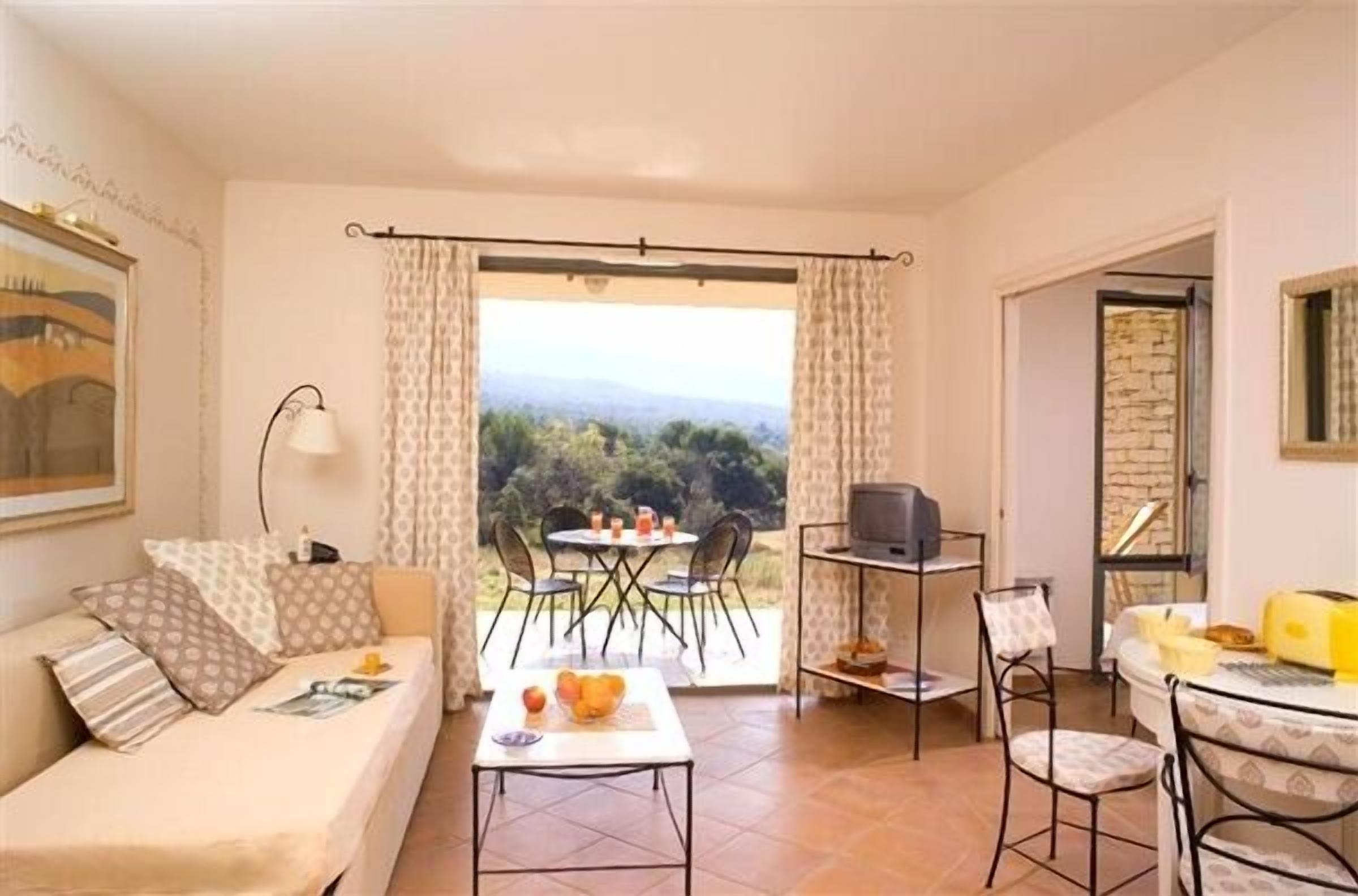 Een gezellige kamer met een bank, een klein tafeltje met fruit, een televisie en een balkon met een tafel en stoelen.