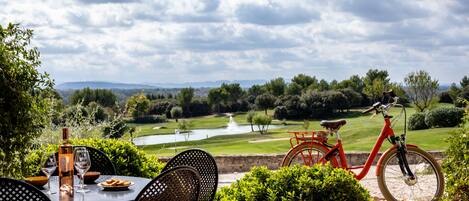 Mesa con sillas, una botella y vasos, con vista a un campo de golf y una bicicleta roja.