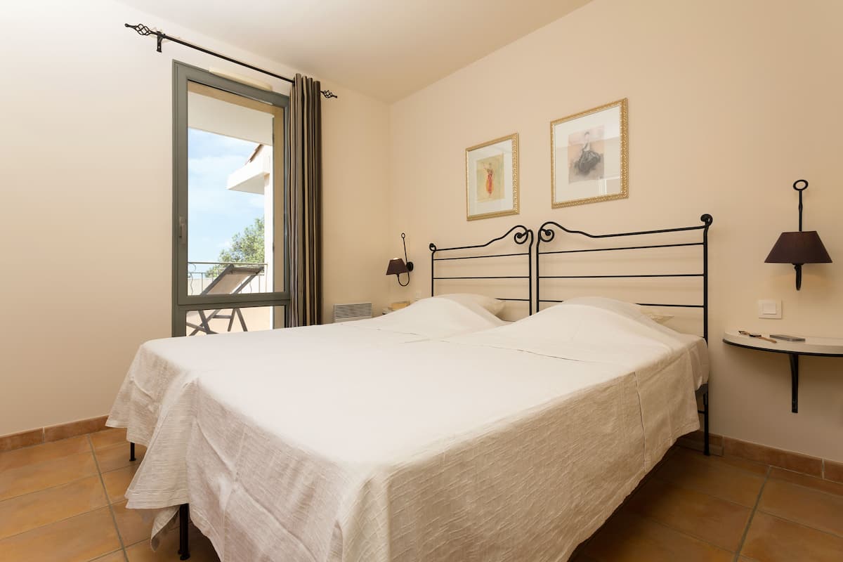 A bedroom with a bed, a nightstand, a lamp, and a window with curtains.