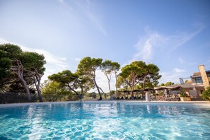 A swimming pool with clear blue water, surrounded by trees and a building with outdoor seating. - Madame Vacances Résidence Provence Country Club (Saumane-de-Vaucluse)
