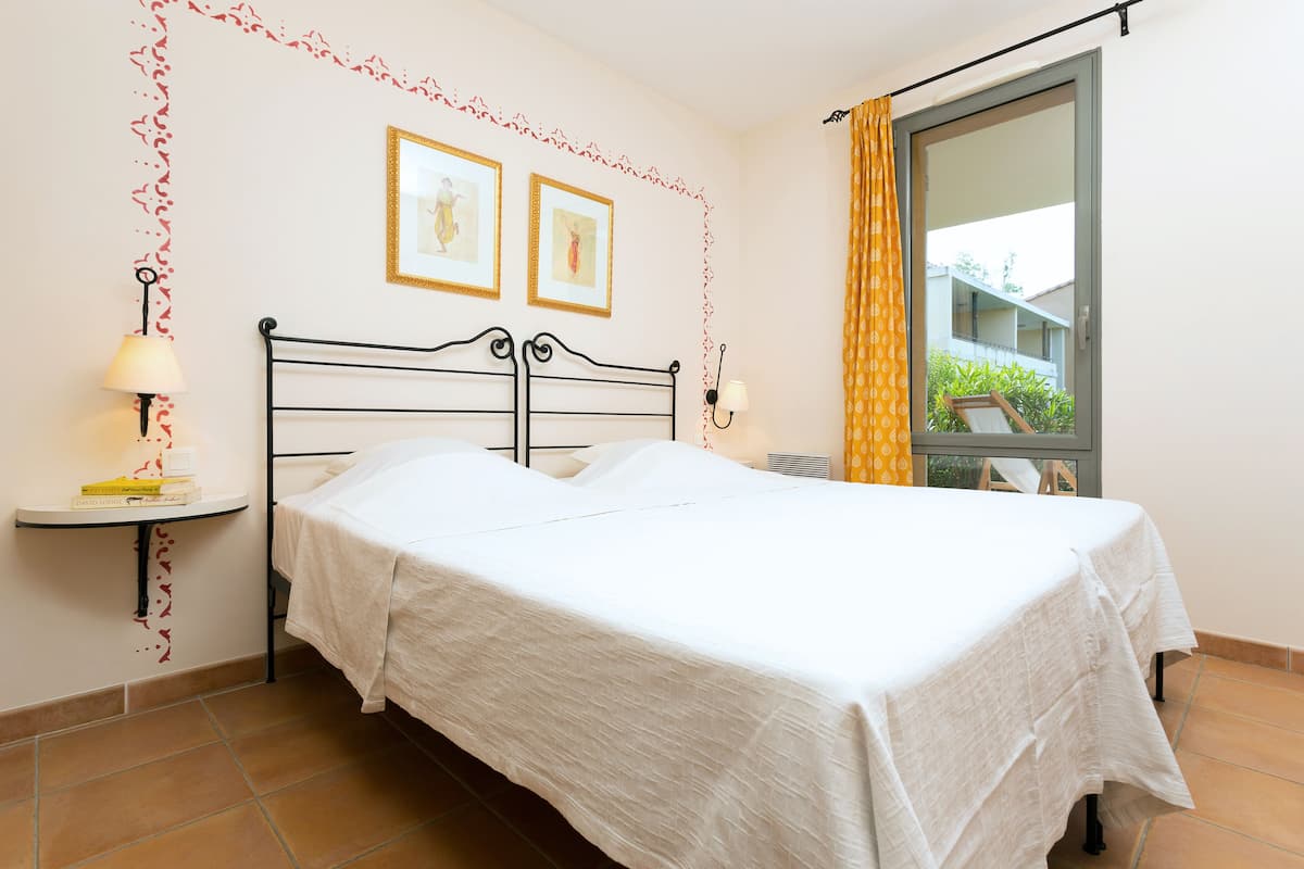 A neatly made bed with white linens, a bedside table with a lamp, and two framed pictures on the wall.