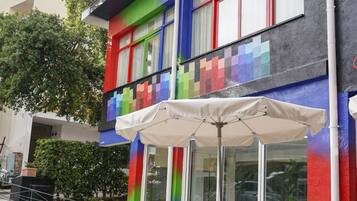A modern building with colorful exterior, large windows, and outdoor seating area with a white umbrella.