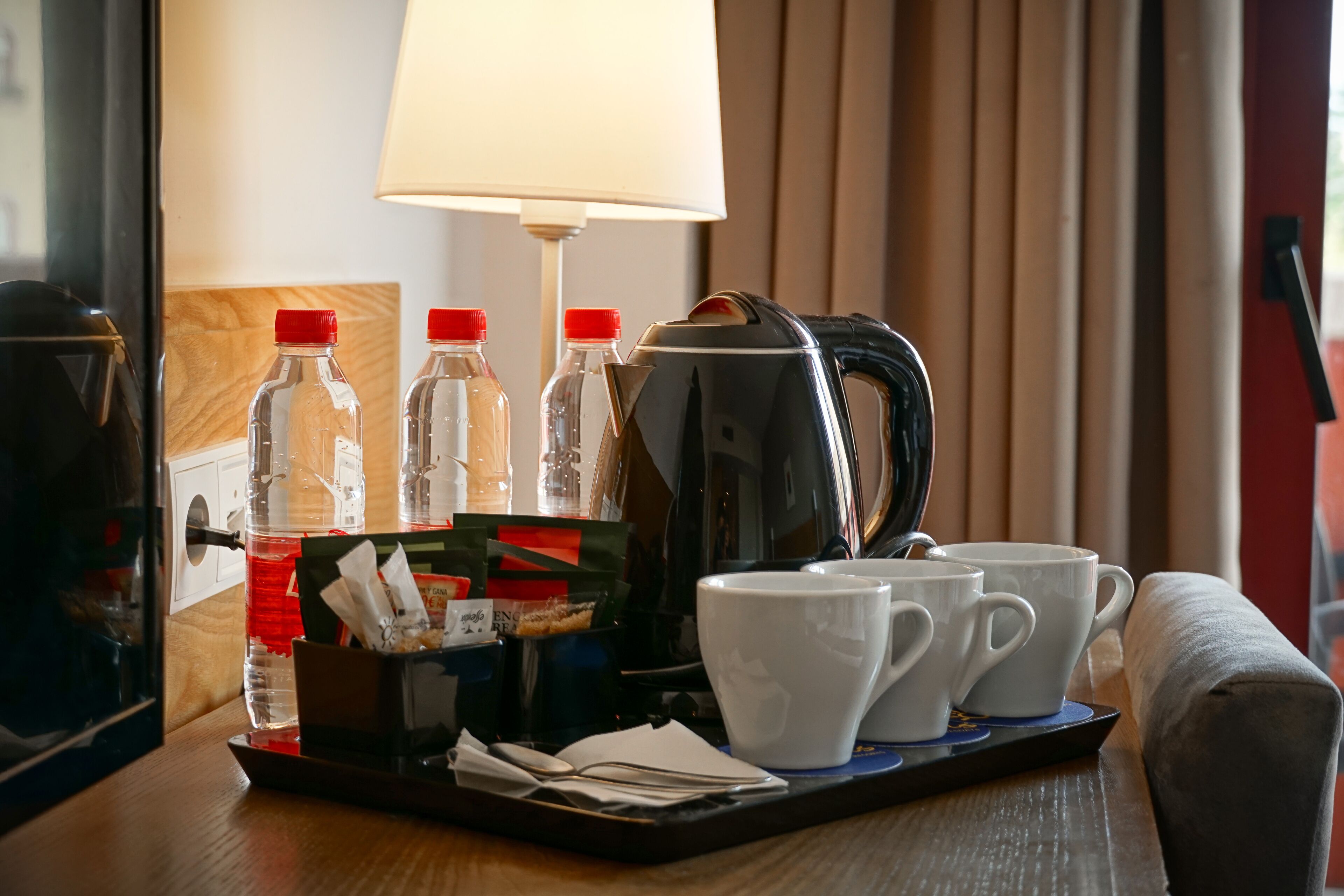 A hotel room with a coffee maker, two cups, and two bottles on a tray.