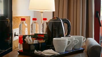 Una habitación de hotel con una cafetera, dos tazas y dos botellas sobre una bandeja.