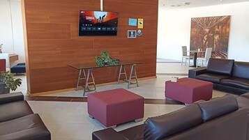 A modern lobby with leather sofas, a glass coffee table, and a TV displaying 'LA VUELTA'.