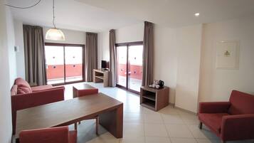 Una sala de estar moderna con una mesa de comedor, sofás rojos, un televisor y un balcón con cortinas.