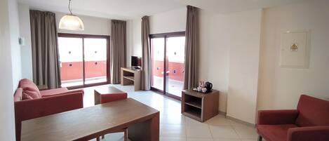 A modern living room with a dining table, red sofas, a TV, and a balcony with curtains.