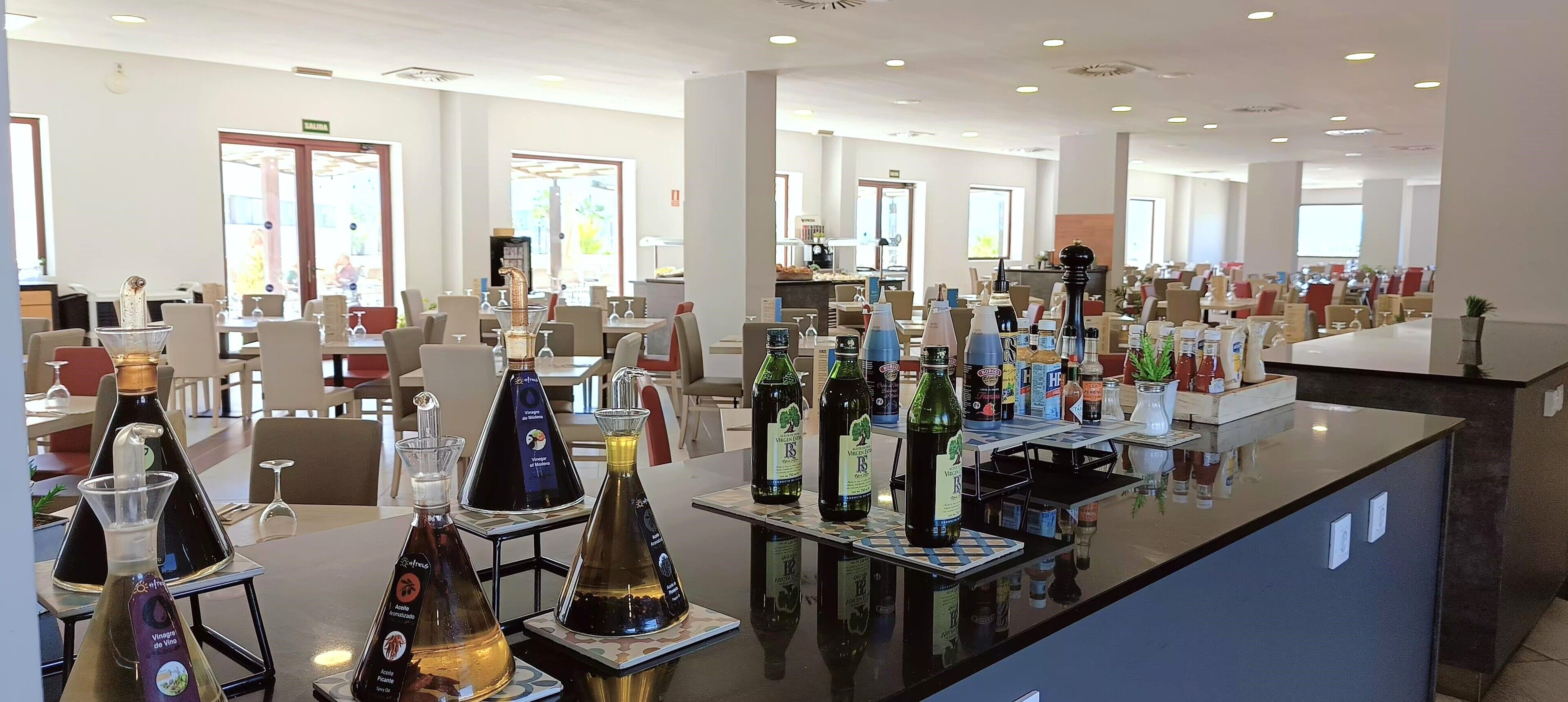 A hotel lobby with multiple dining tables, chairs, and a variety of bottles on display.