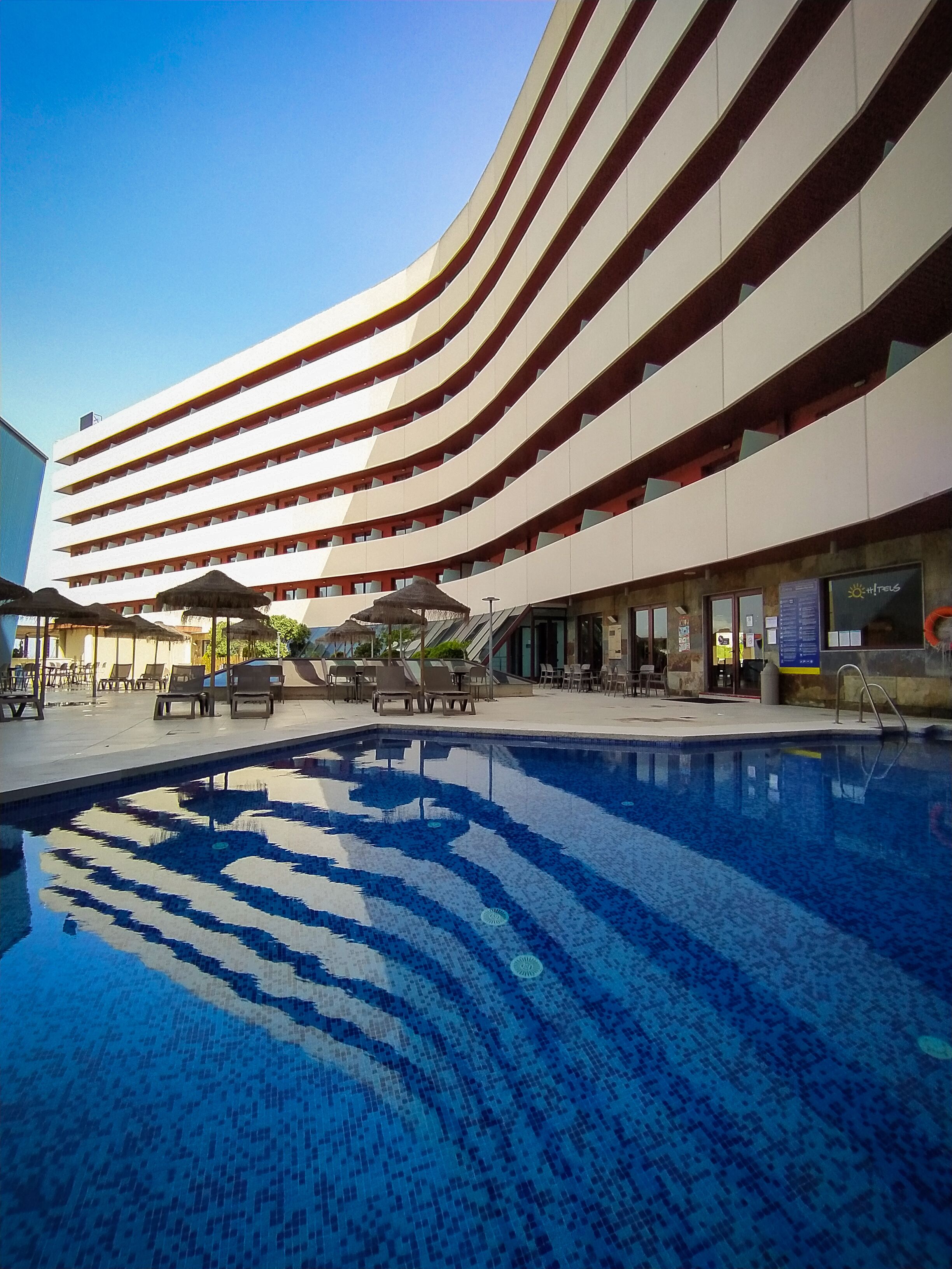 Un hôtel moderne à la façade incurvée, doté d’une piscine et d’espaces de détente en plein air.