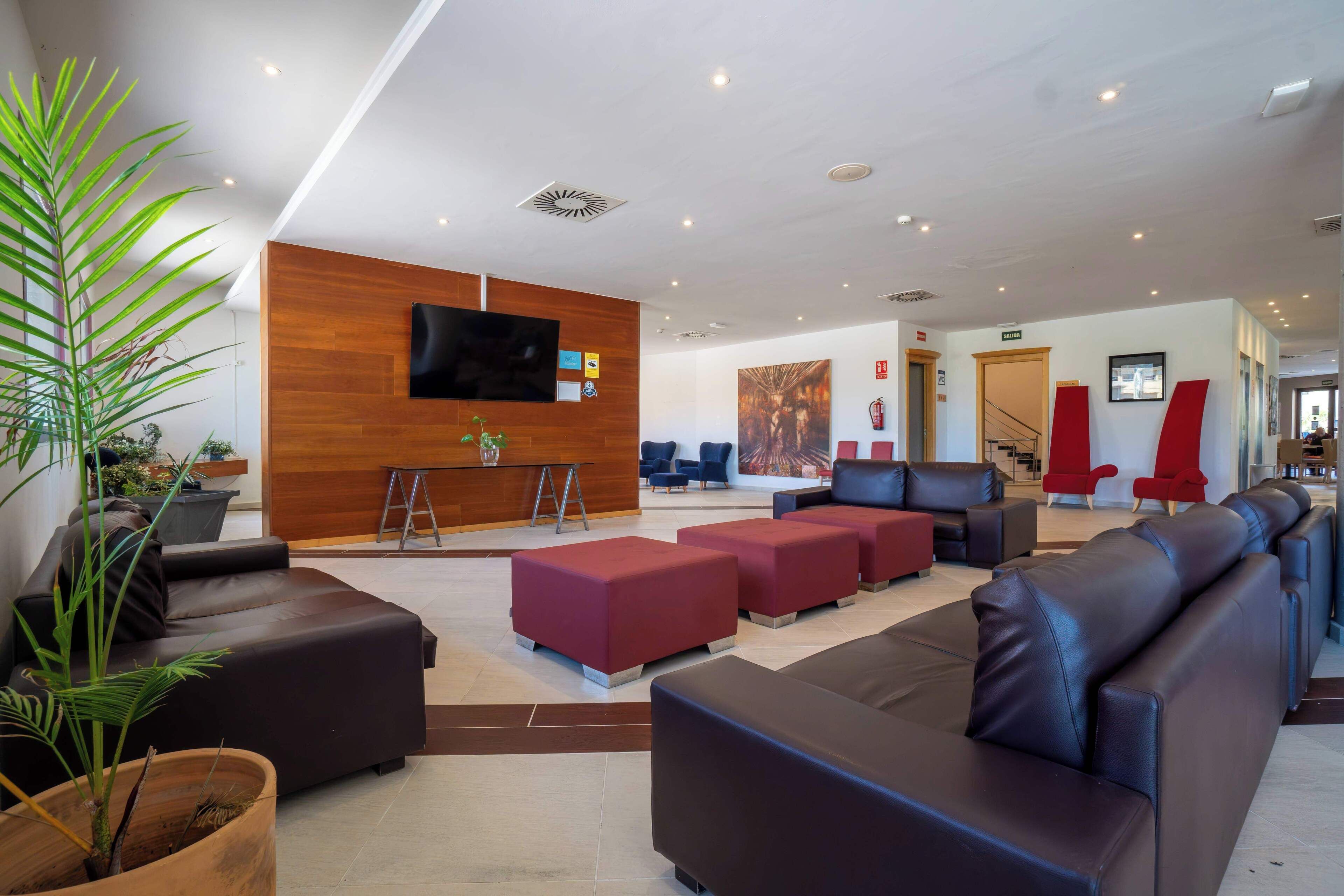 Eine moderne Hotelhalle mit Ledersofas, roten Hocker, einem Holzbüro und einem Flachbildfernseher.