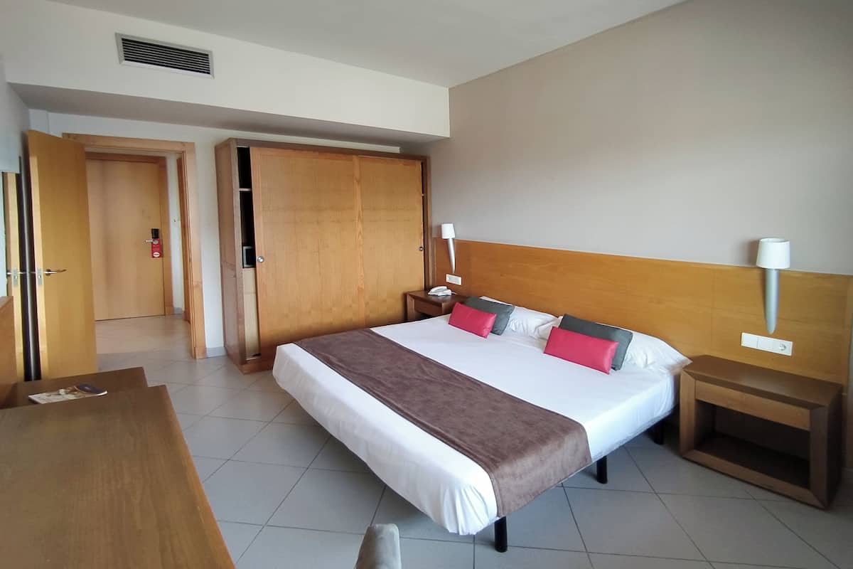 A hotel room with a large bed, wooden headboard, bedside tables, and a wooden wardrobe.