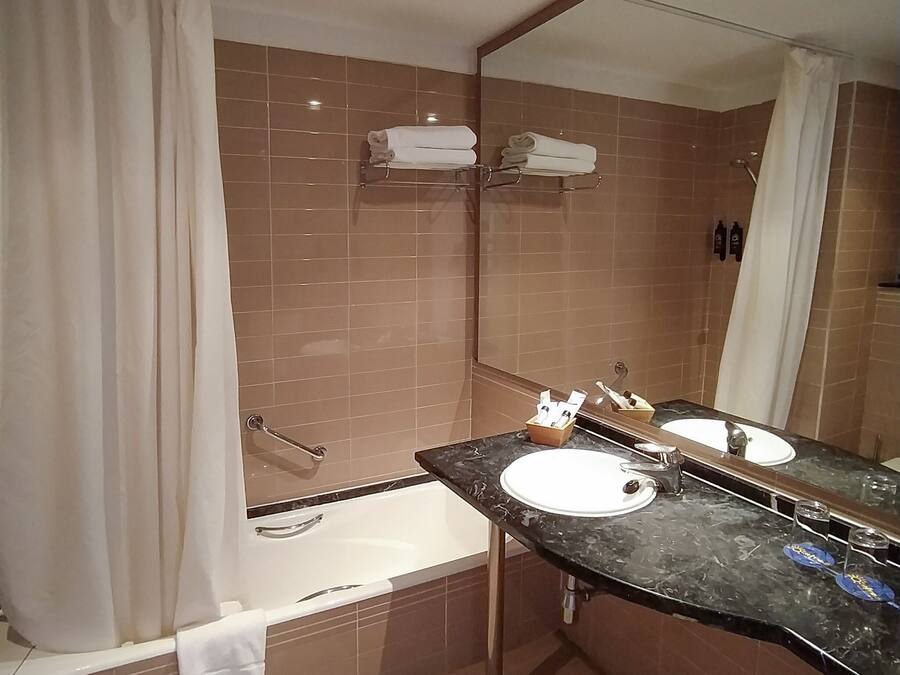 A bathroom with a bathtub, two sinks, a large mirror, and a towel rack.