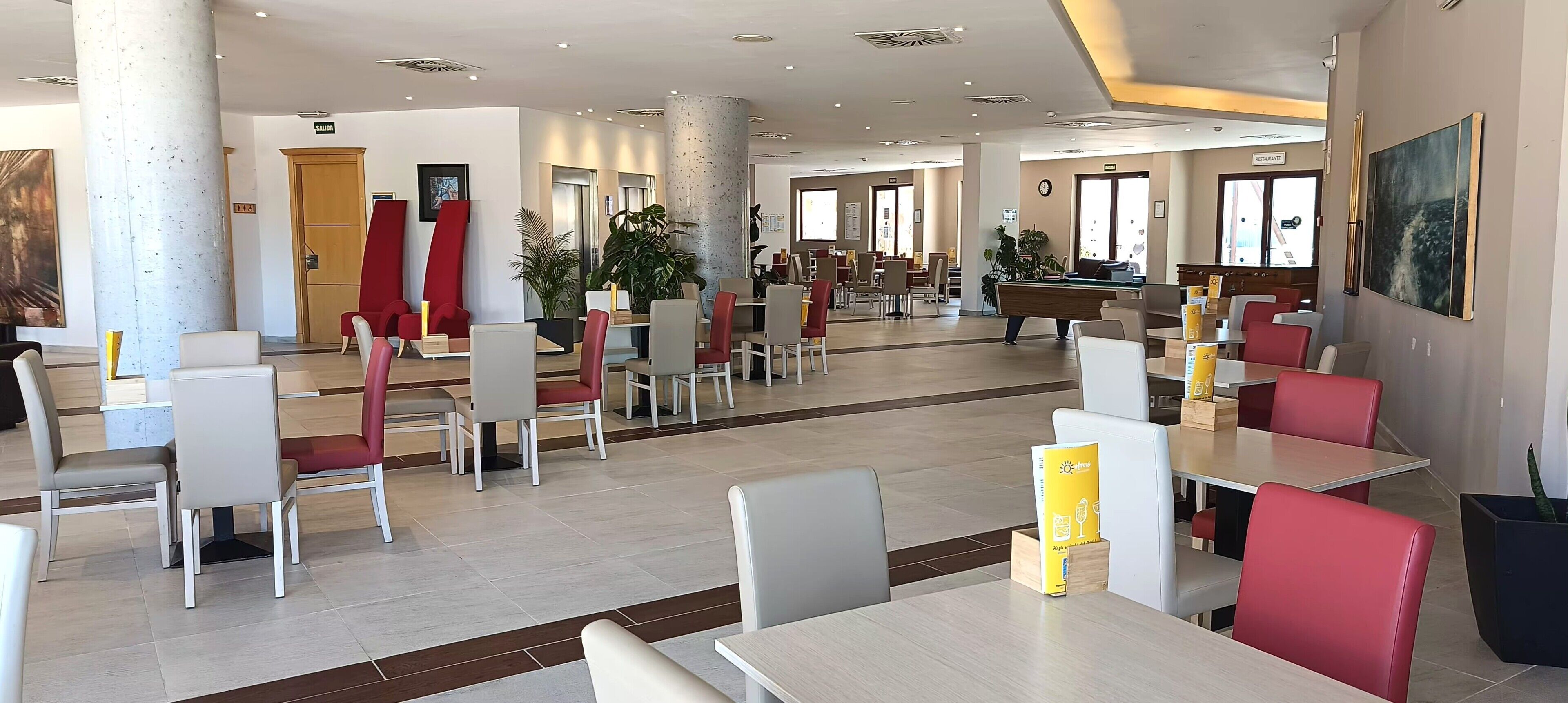 Un amplio vestíbulo de hotel con varias zonas de restauración, una mesa de billar y un letrero de restaurante.
