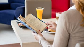 Una persona leyendo un libro en una mesa con un vaso de jugo de naranja y un plato de comida.