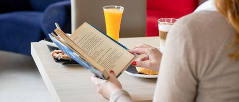 A person reading a book at a table with a glass of orange juice and a plate with food.