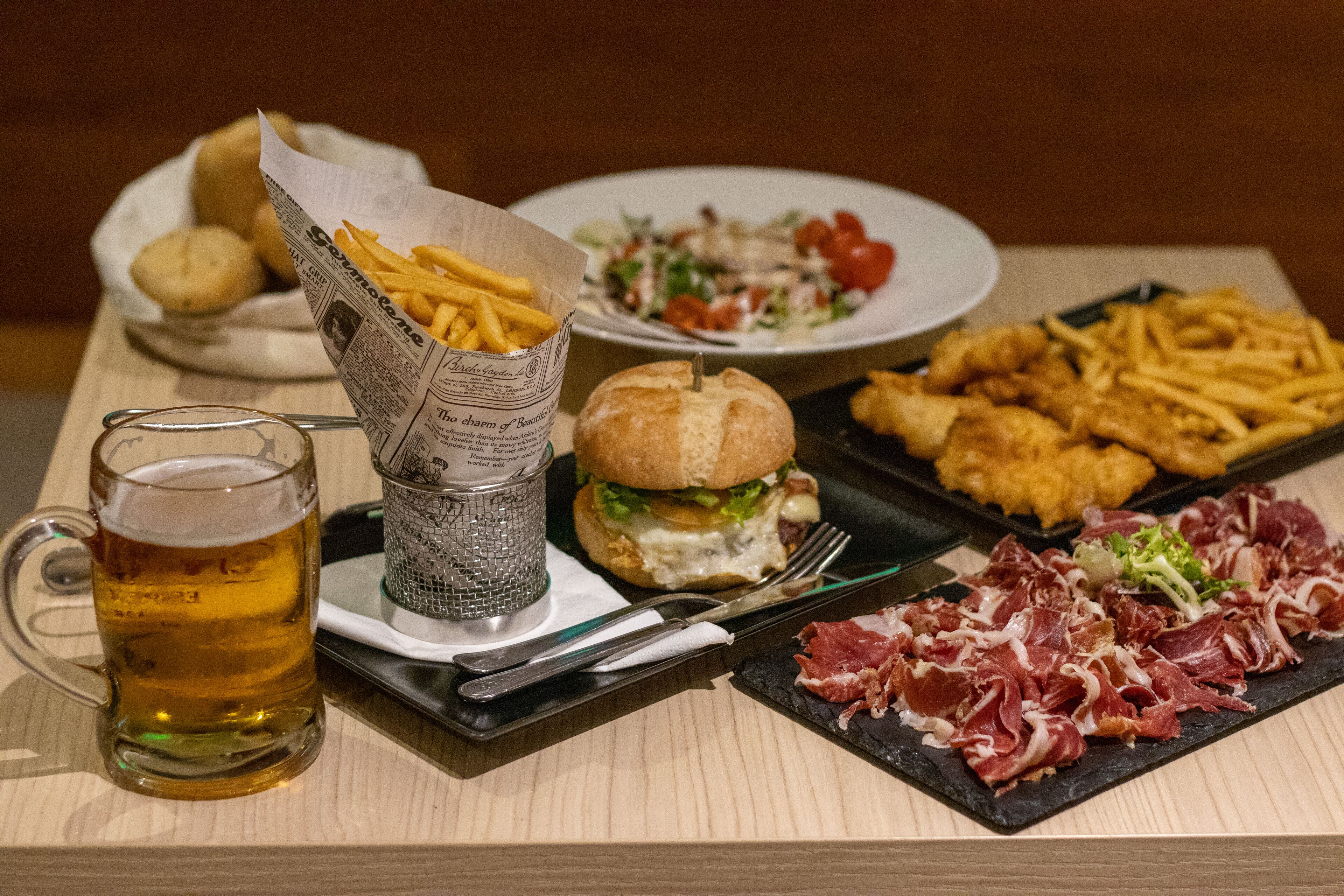 Un plateau avec un hamburger, des frites et de la viande, une chope de bière et une assiette à salade.