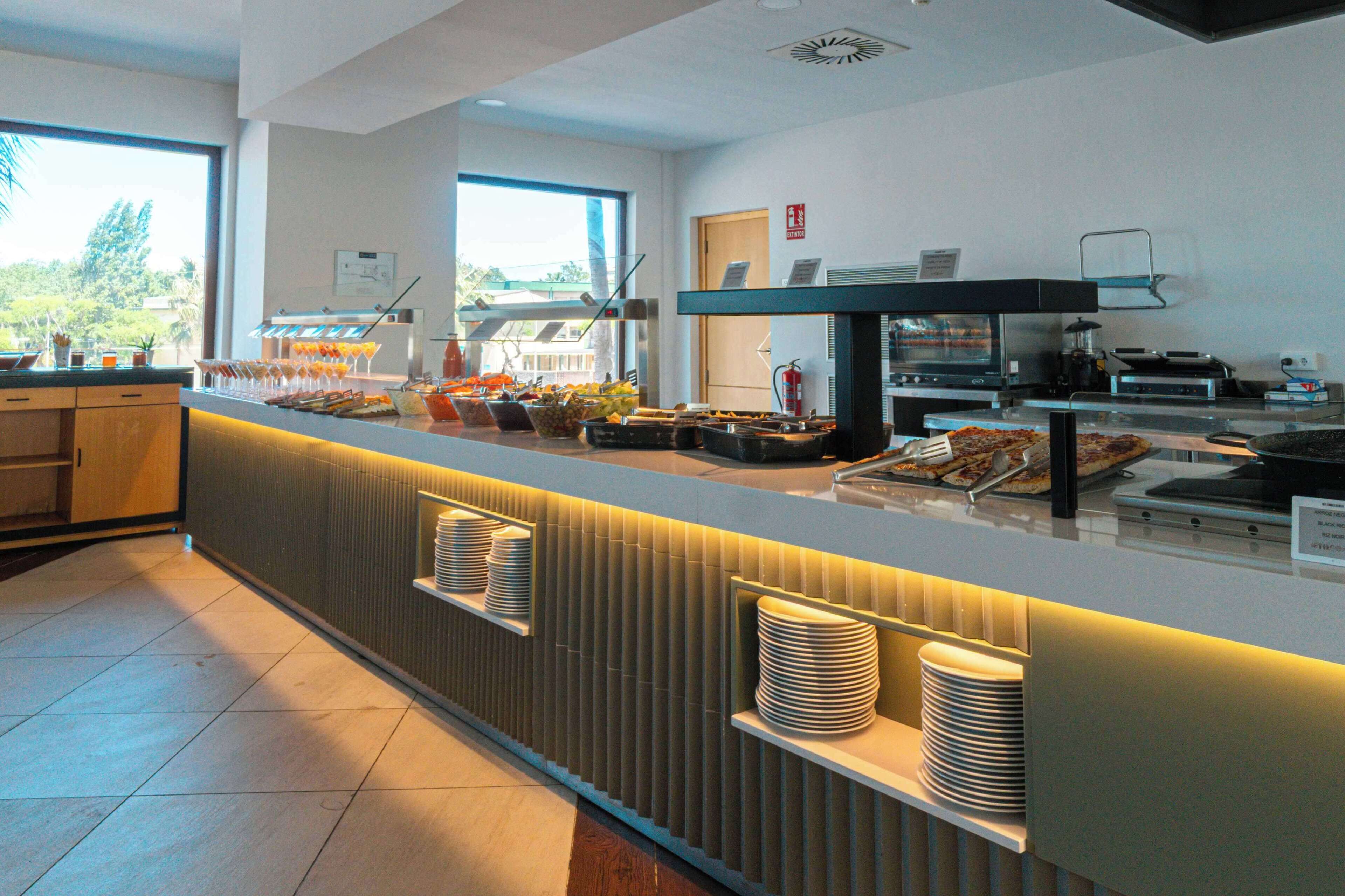 A modern breakfast bar with a variety of food items and beverages, a coffee machine, and a view of the outdoors.