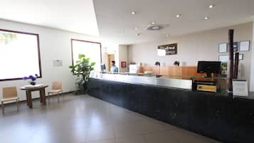 Un espace d’accueil doté d’un comptoir en marbre noir, de chaises en bois, d’une plante en pot et d’une enseigne indiquant le nom de l’hôtel.
