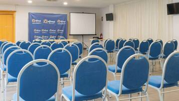 A conference room with rows of blue chairs, a whiteboard, and a projector screen.
