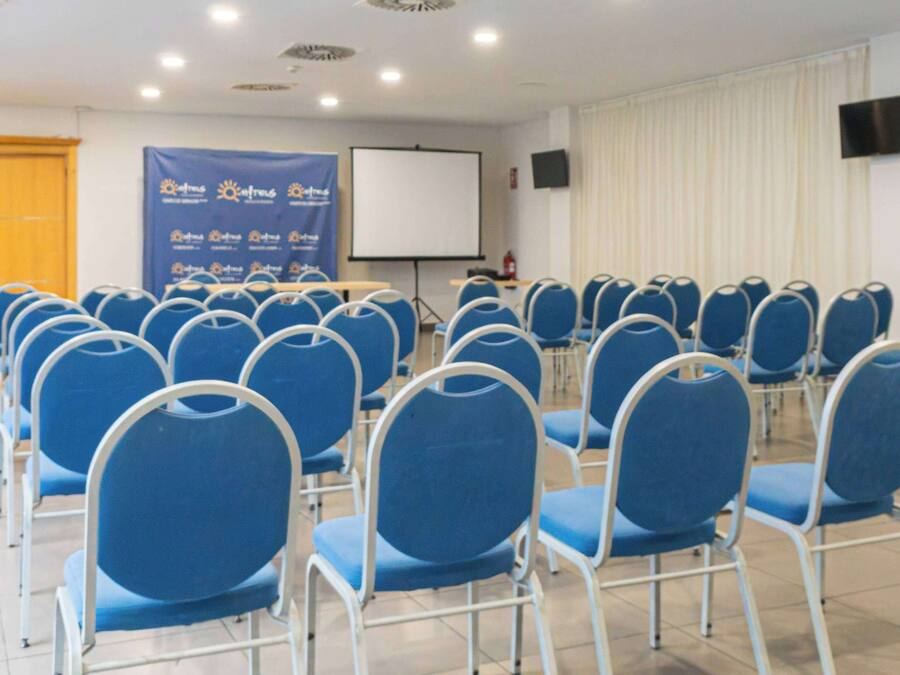 A conference room with rows of blue chairs, a whiteboard, and a projector screen.