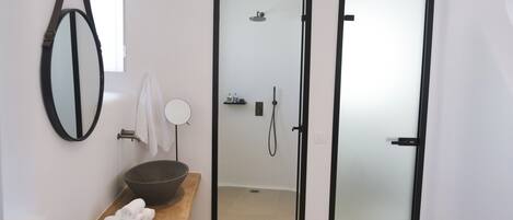A modern bathroom with a wooden vanity, a large mirror, a round mirror, and a shower area visible through a frosted glass door.