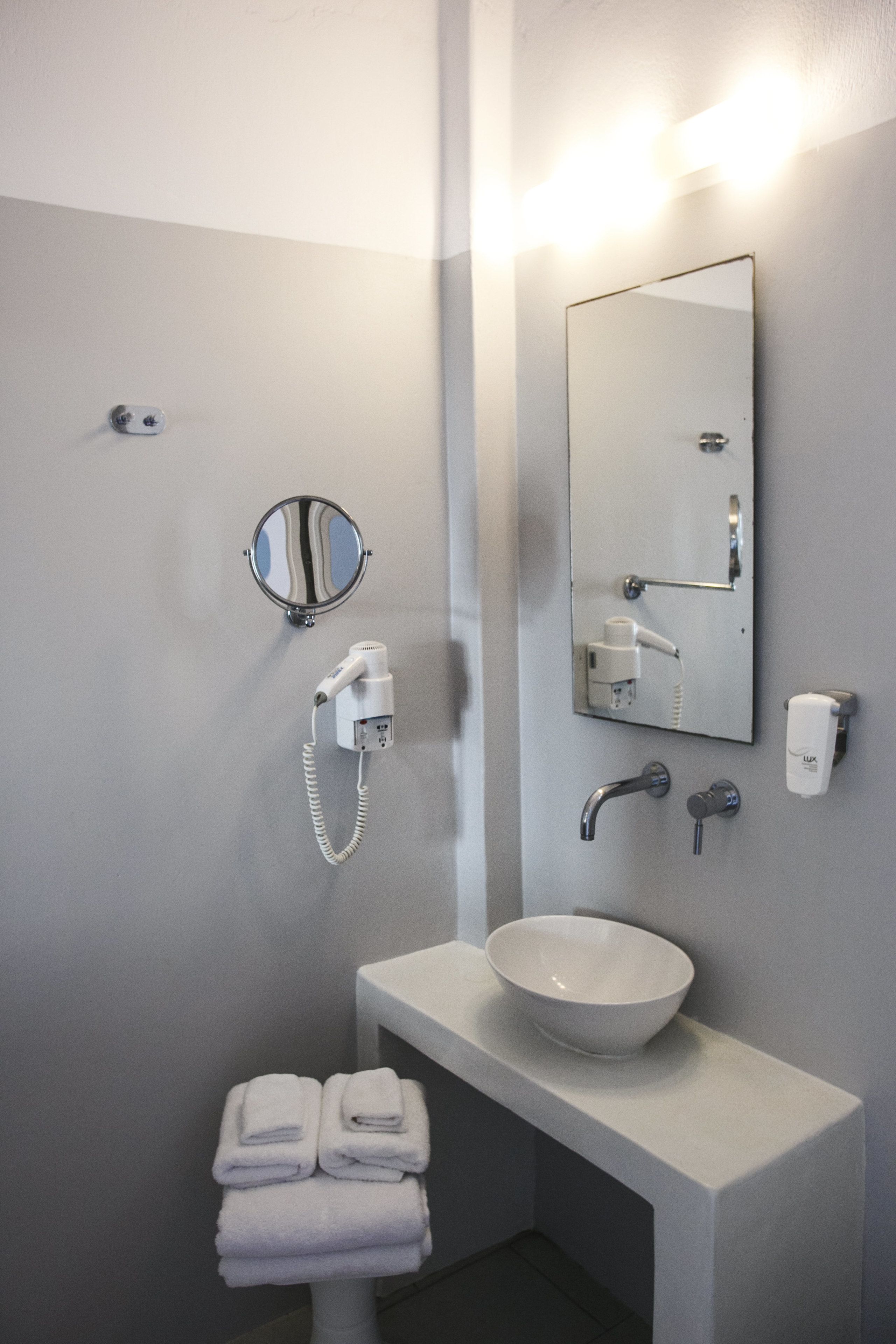 Un baño moderno con un lavabo blanco, un espejo redondo, un secador de pelo y un perchero para toallas.