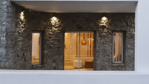 A stone facade with three windows, a hanging light fixture, and a glimpse of a bathroom interior. - Argo Hotel (Mykonos)