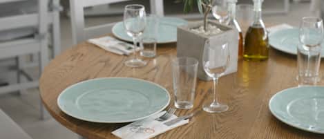 A dining table set with plates, glasses, and a bottle, surrounded by chairs and a potted plant.