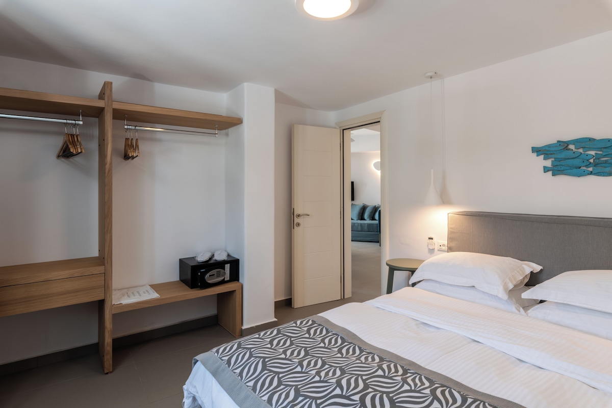 A modern hotel room with a bed, a wooden wardrobe, a bedside table, and a wall-mounted artwork.