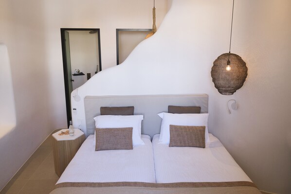 A modern hotel room with a large bed, a bedside table, a hanging light fixture, and a mirror on the wall. - Argo Hotel (Mykonos)