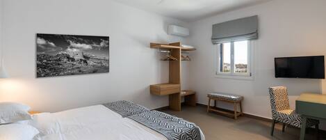 Un dormitorio con cama, escritorio, silla, ventilador de techo, ventana con vistas y televisor montado.