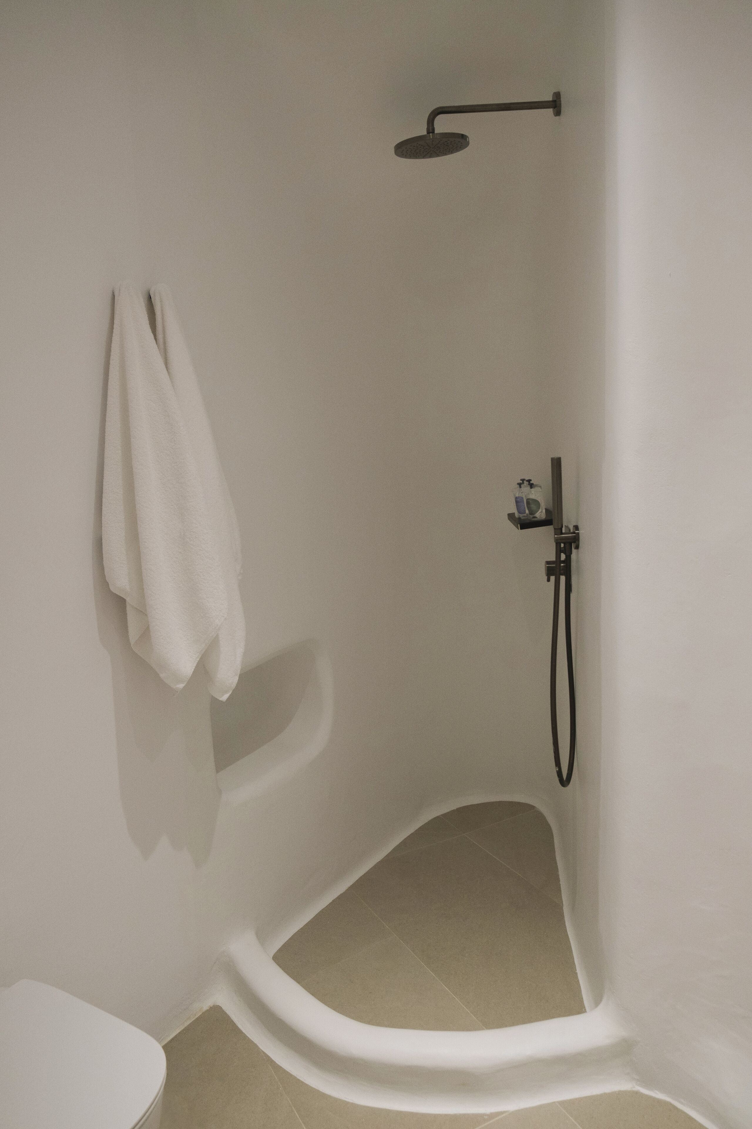Une douche d’angle avec un pommeau de douche à main, une serviette accrochée au mur et des toilettes.