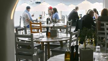 An outdoor dining area with tables and chairs, umbrellas, and a view of the sea.
